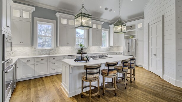 A spacious kitchen with white cabinetry, a large island with bar stools, and pendant lighting.