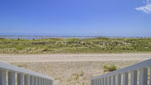 A beach view with a white fence, sandy beach, and grassy dunes. - 103 B Port O Call by Avantstay Direct Beach Access Screened In Porch! (Isle of Palms)
