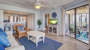 A spacious living room with a sofa, a coffee table, and a television. There is a sliding glass door leading to a balcony. - 103 B Port O Call by Avantstay Direct Beach Access Screened In Porch! (Isle of Palms)