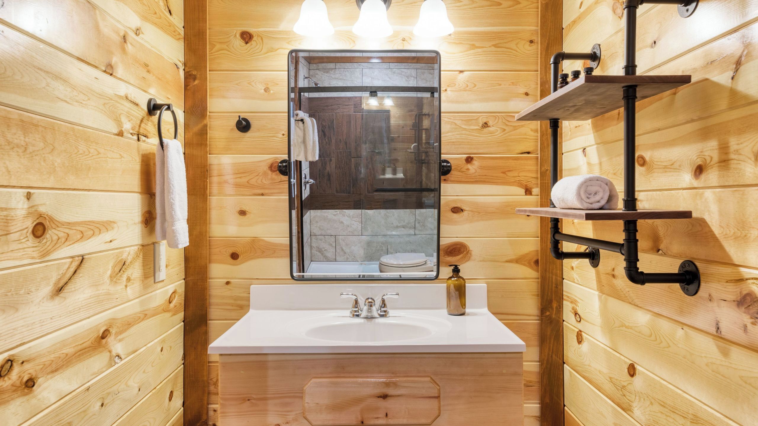 A wooden-paneled bathroom with a white sink, a mirror, and a shelf with a towel.
