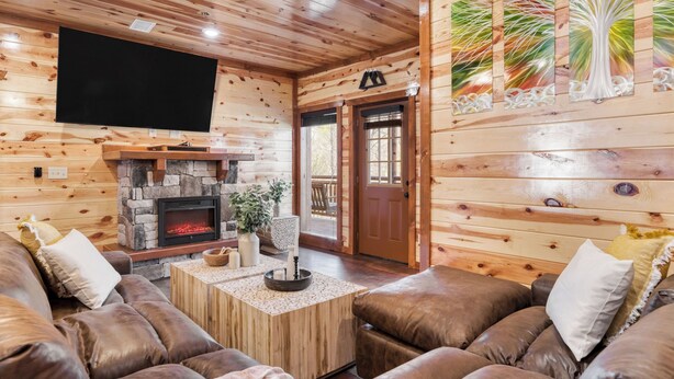 A wooden interior with a fireplace, leather couches, a flat-screen TV, and a door with a logo. - Boon by Avantstay 40-guest Luxe Smokies Retreat (Sevierville)