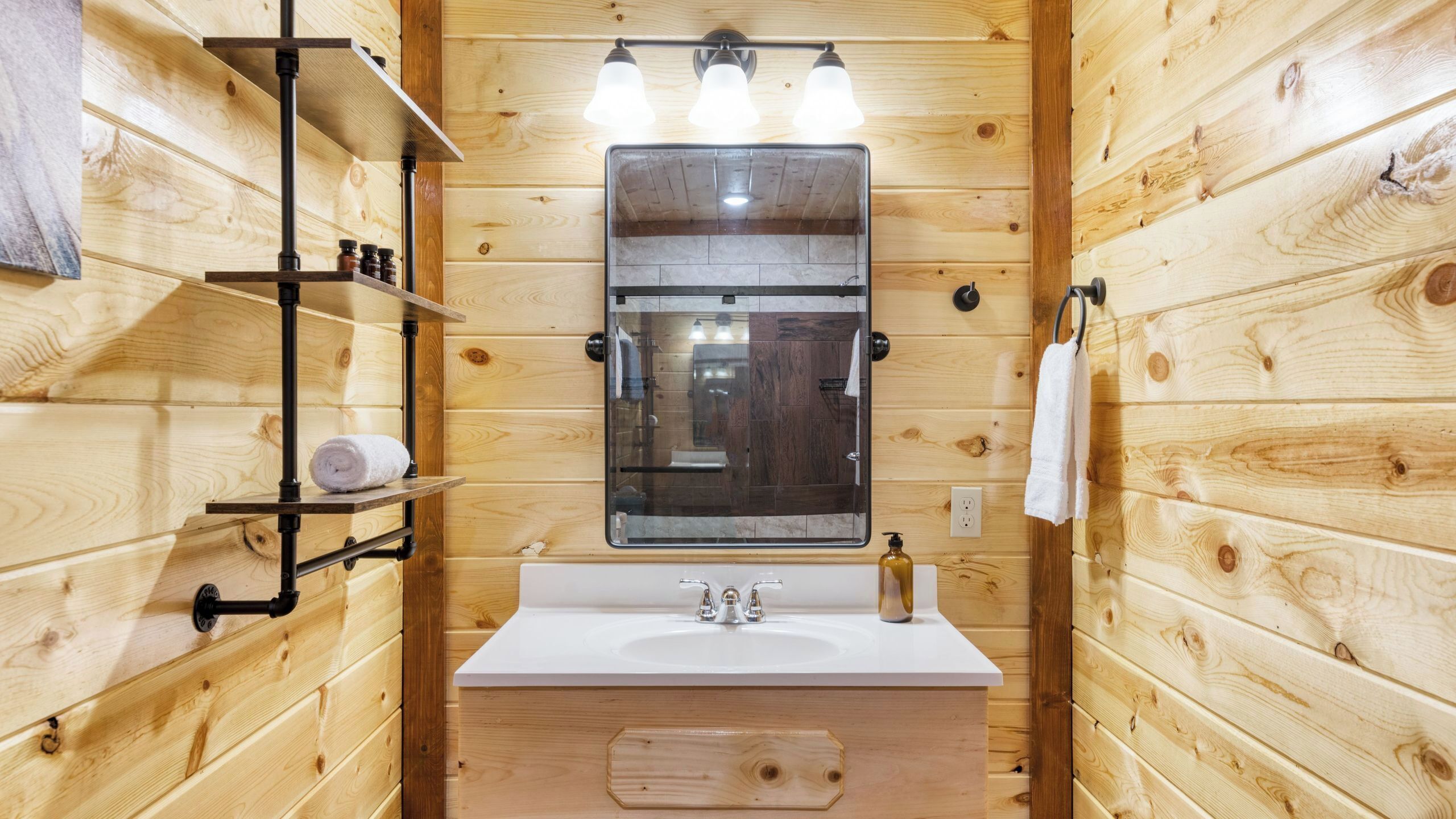 A wooden cabin bathroom with a white sink, a mirror, and a shelf with toiletries.