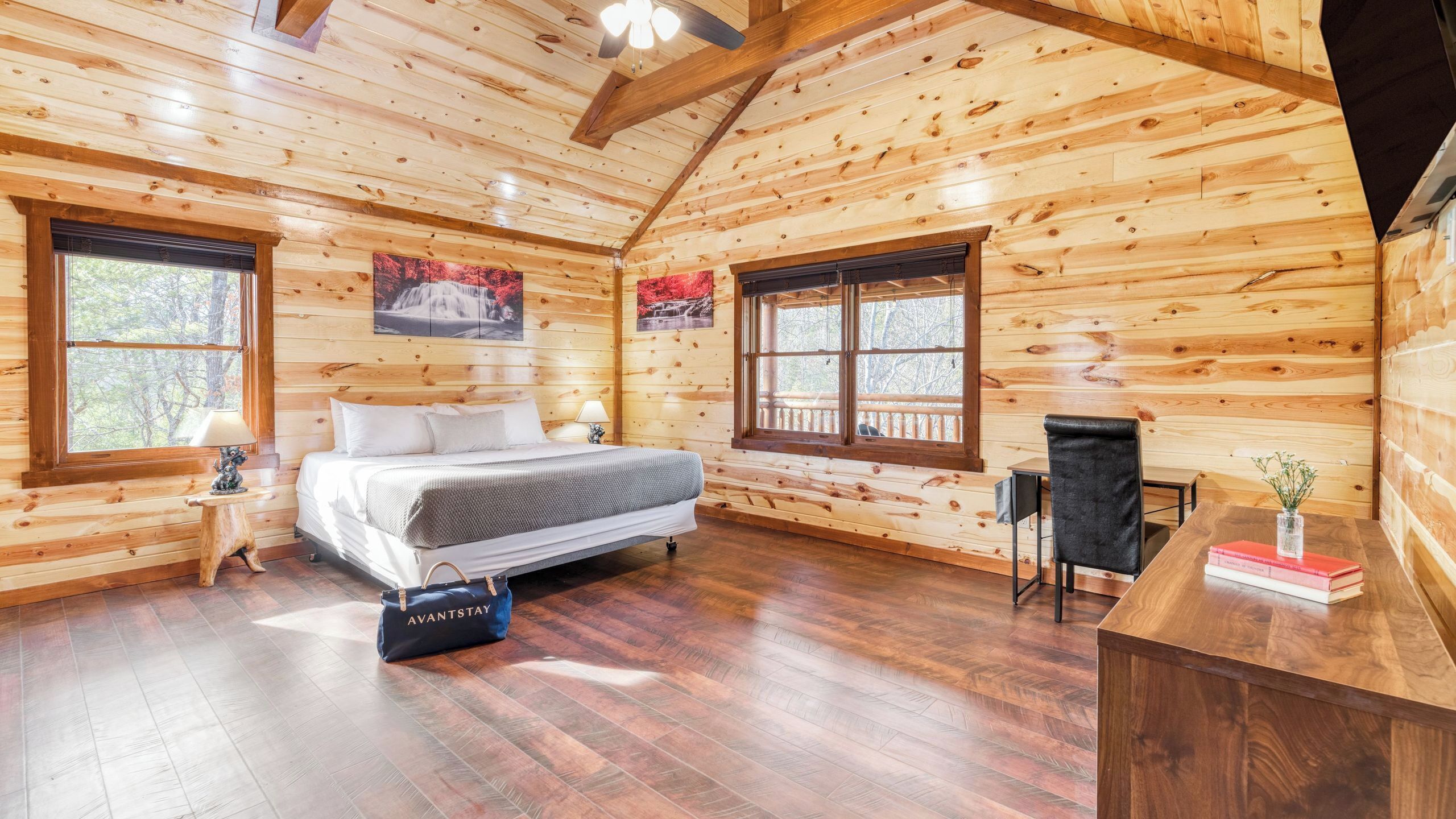 A log cabin bedroom with a bed, two windows, a fireplace, and a desk.