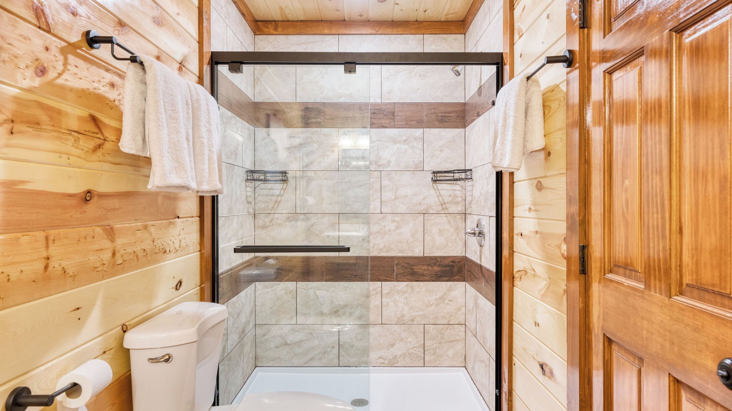 A wooden-paneled bathroom with a shower, toilet, and towel rack.
