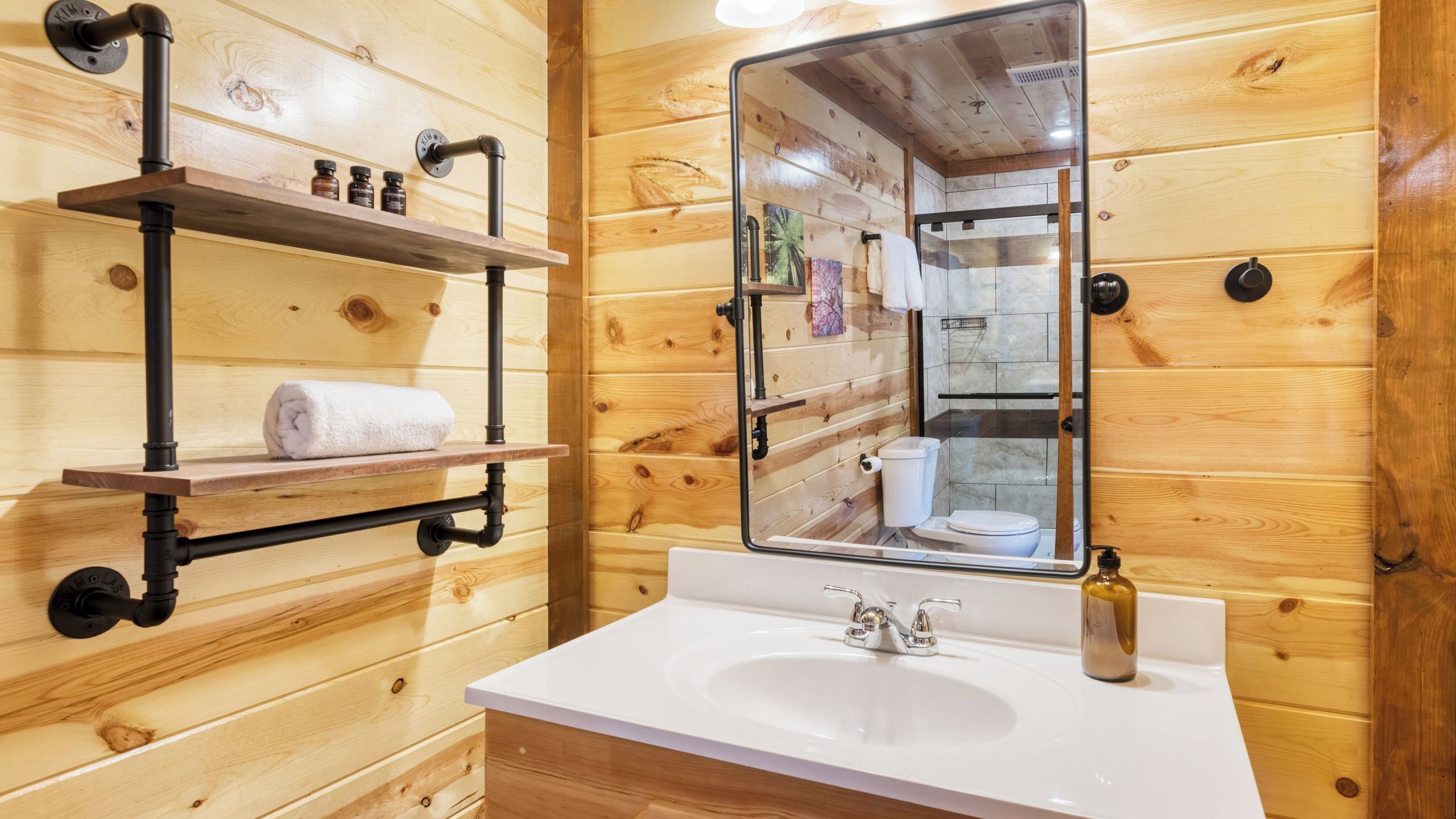 A wooden cabin bathroom with a white sink, a mirror, and a towel rack.