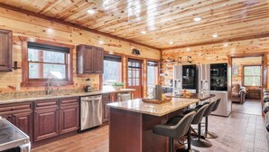 A modern kitchen with wooden paneling, stainless steel appliances, and a central island with bar stools. - Boon by Avantstay 40-guest Luxe Smokies Retreat (Sevierville)