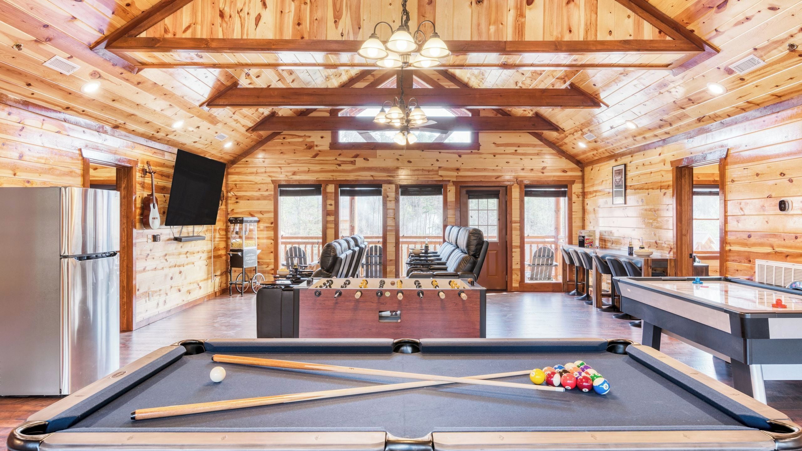 A wooden cabin with a pool table, seating area, and a foosball table.