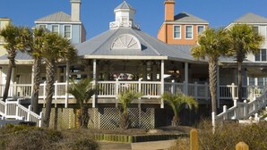 A beachfront property with a covered porch, multiple balconies, and palm trees. - 1403 Ocean Club by Avantstay Beach Home w/ Great Kitchen (Isle of Palms)