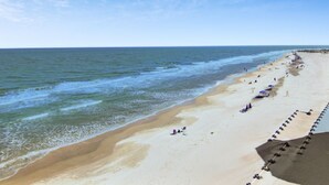 A beach with a long stretch of sand, a few umbrellas, and people. - 1403 Ocean Club by Avantstay Beach Home w/ Great Kitchen (Isle of Palms)