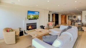 A modern living room with a fireplace, a television mounted above it, and a cozy seating area with a sofa and armchairs. - 1403 Ocean Club by Avantstay Beach Home w/ Great Kitchen (Isle of Palms)