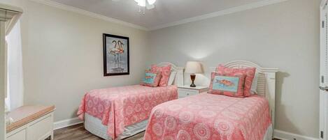 A bedroom with two beds, a nightstand, a framed picture on the wall, and a ceiling fan.