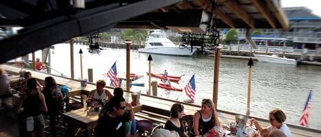A boat with tables and chairs, docked near a marina with boats and American flags.