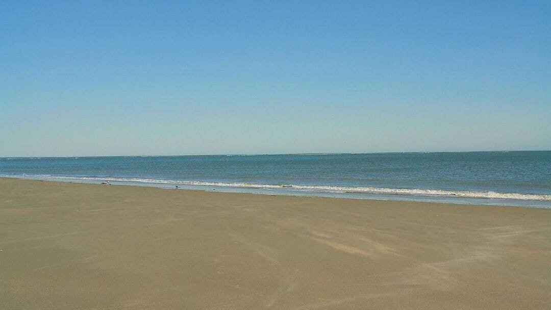 Una playa con cielo despejado y mar tranquilo.