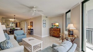 A spacious living room with a white ceiling fan, a dining area with a wooden table, and a kitchen in the background. - 216 C Shipwatch by Avantstay Shared Pool + Ocean Views + Walk to the Beach (Isle of Palms)