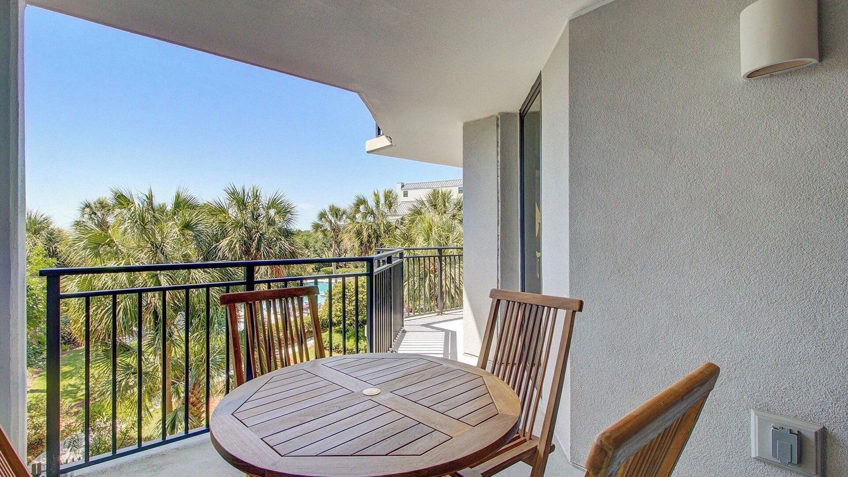 A balcony with a round table and two chairs, overlooking a pool and palm trees.