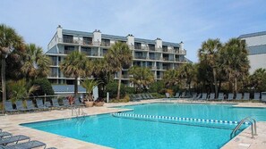 A hotel with a swimming pool, palm trees, and lounge chairs.