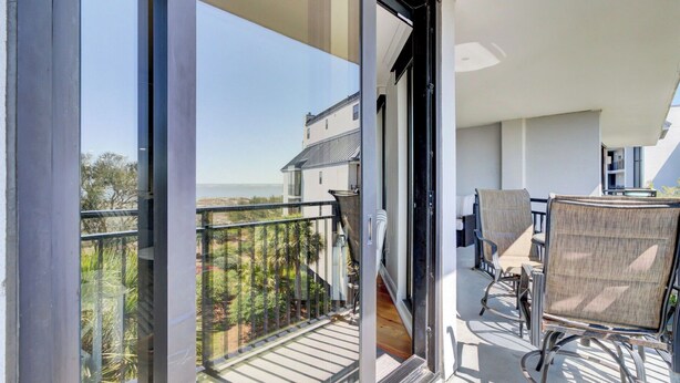 A balcony with a view of a building and trees, a chair, and a table. - 314 C Shipwatch by Avantstay Oceanfront With Ocean View (Isle of Palms)