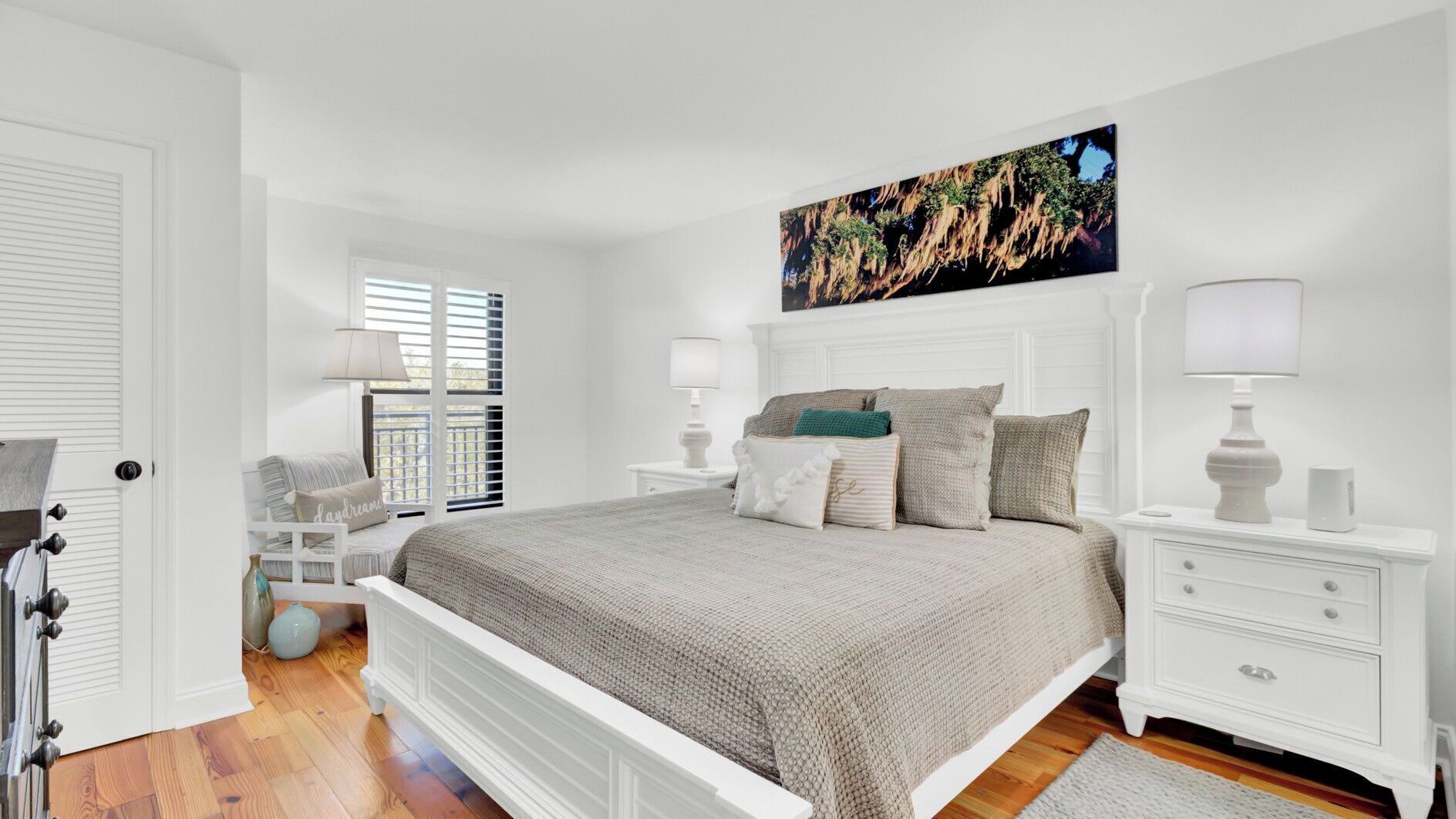 A bedroom with a bed, nightstands, a lamp, a painting, and a window with blinds.