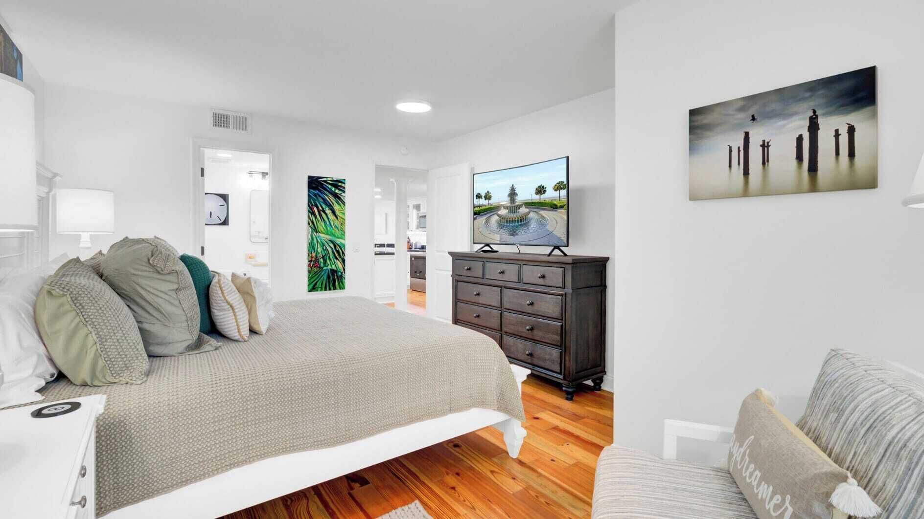 A modern bedroom with a large bed, a dresser, a TV, and a painting on the wall.