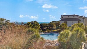 A pool surrounded by tropical vegetation and a building with a sloped roof. - 314 C Shipwatch by Avantstay Oceanfront With Ocean View (Isle of Palms)