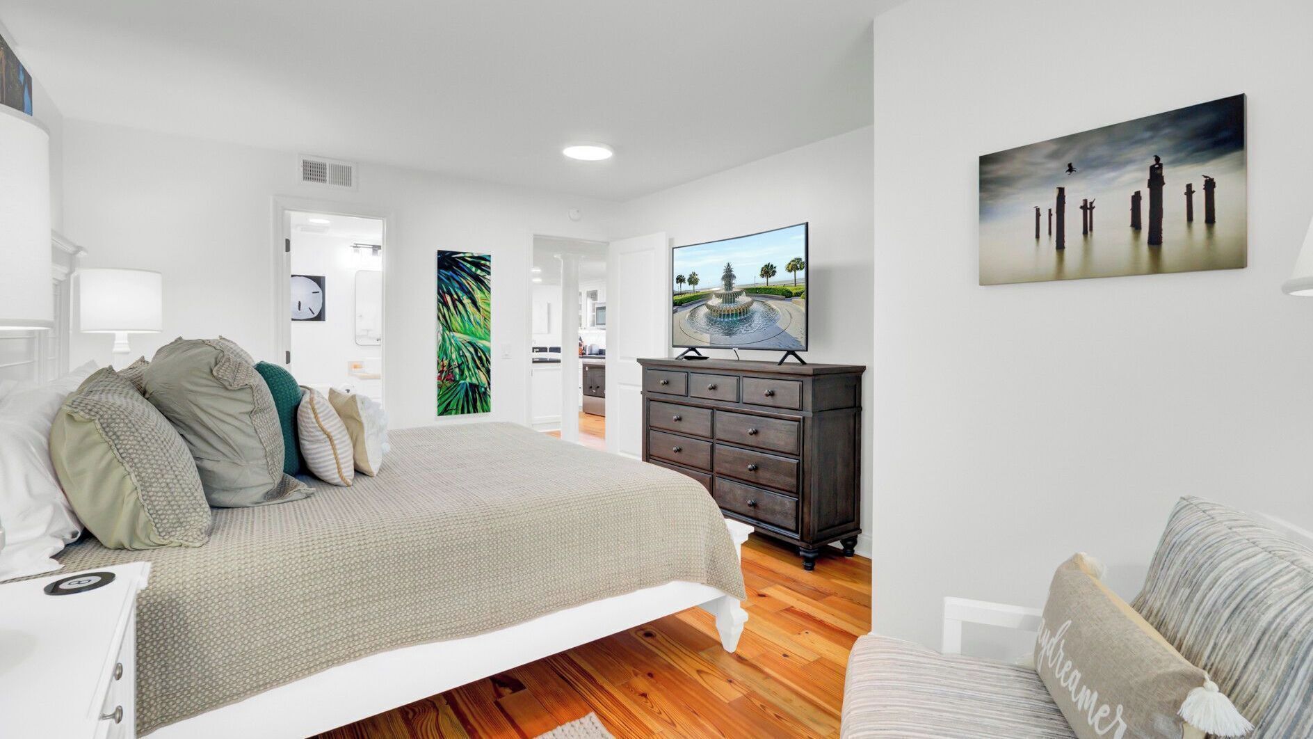 A bedroom with a bed, dresser, TV, and artwork.