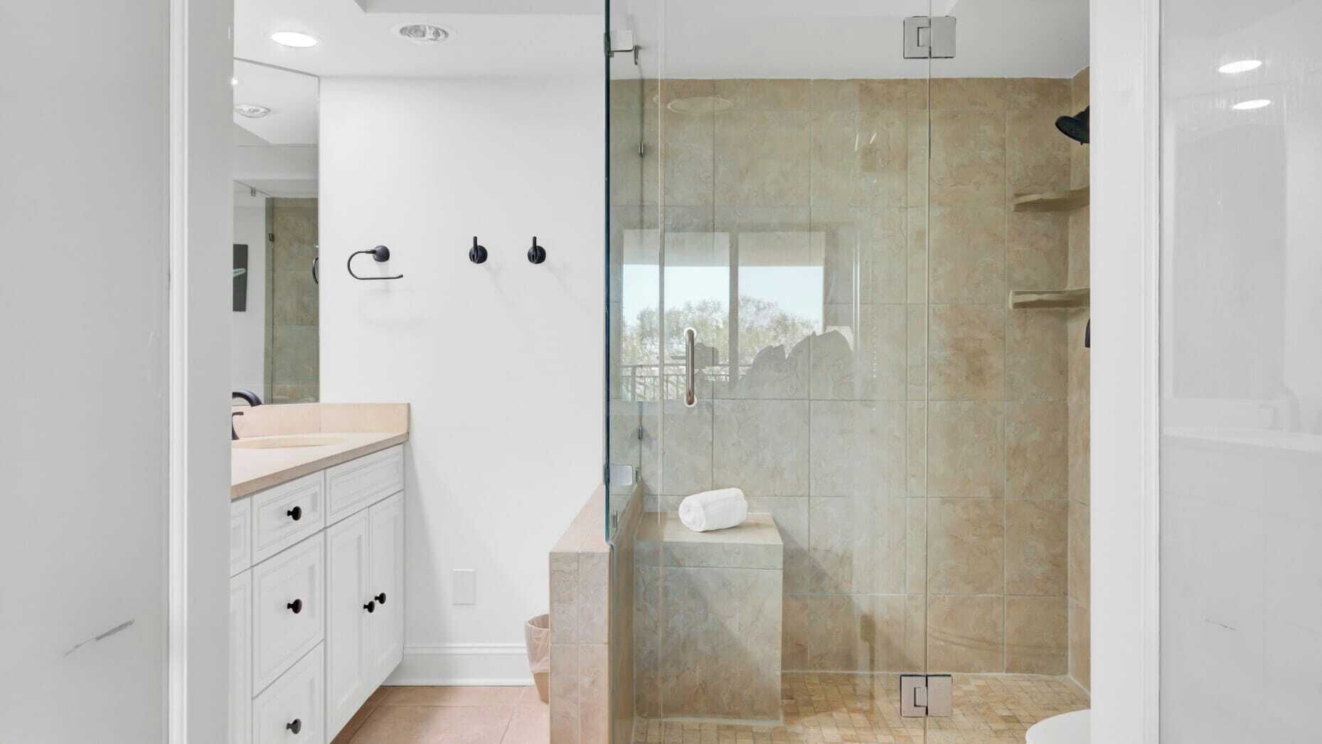 A modern bathroom with a glass-enclosed shower, a white vanity with drawers, and a visible towel on a shelf.
