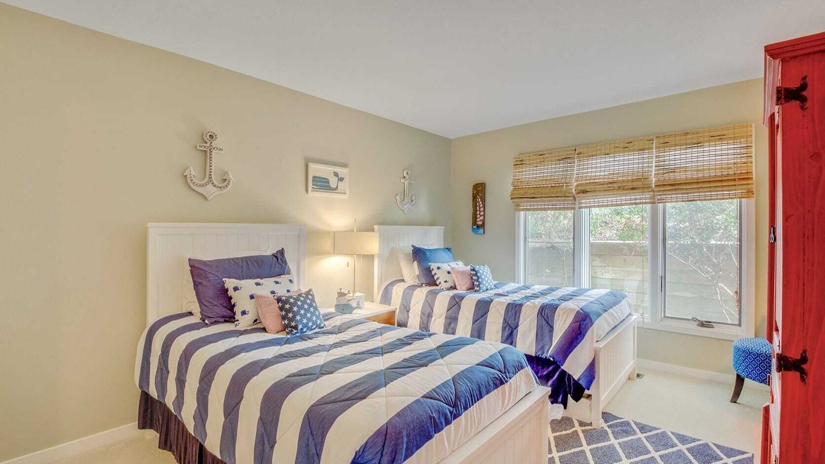 A bedroom with two beds, a window with blinds, and nautical-themed decor.