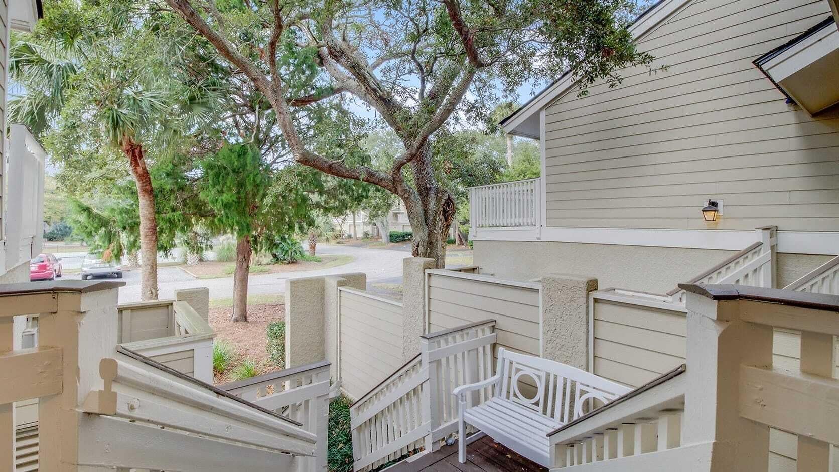 A residential building with a staircase leading to a porch, surrounded by trees and a clear sky.