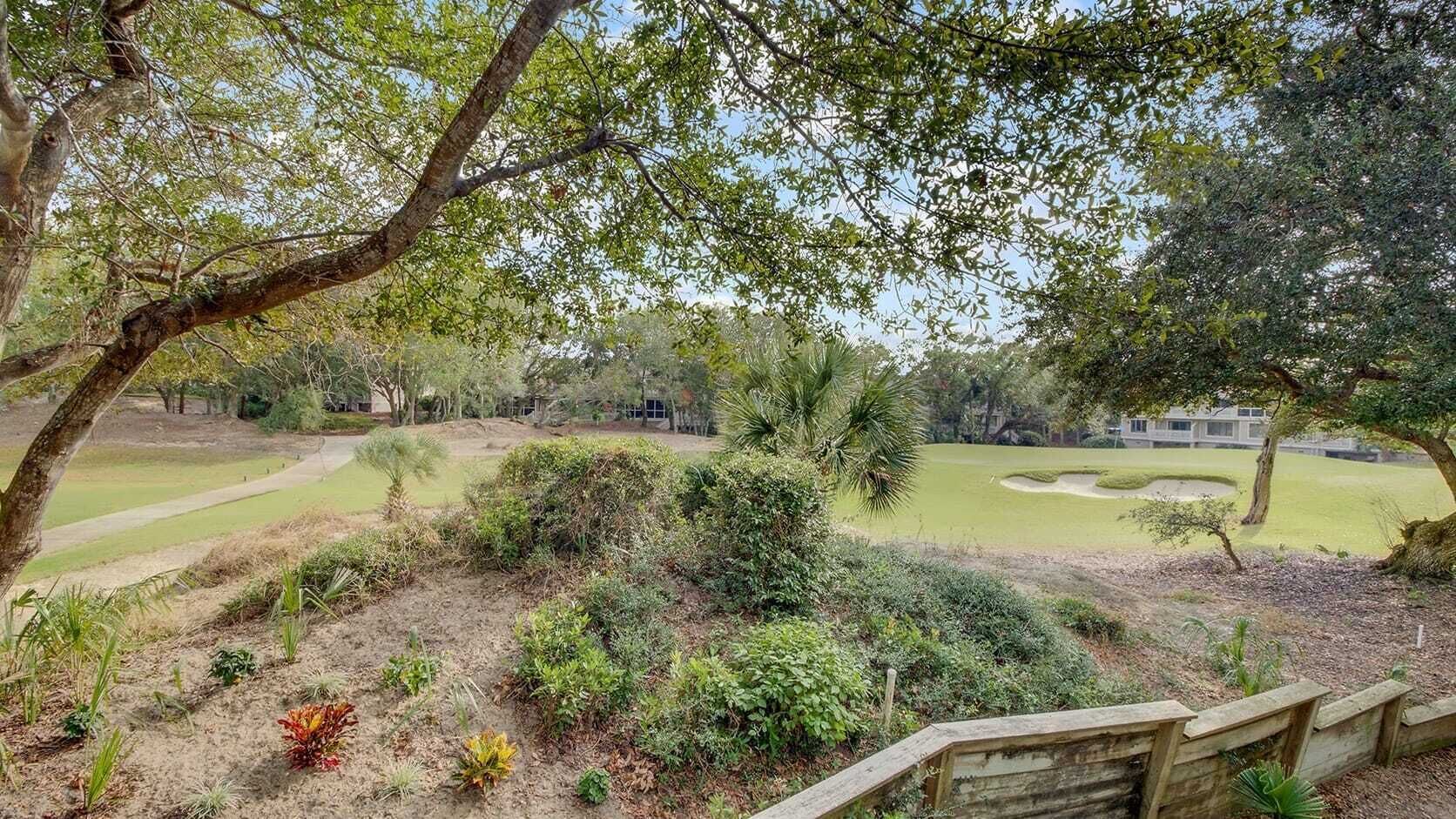 Jardim ajardinado com diversas árvores e arbustos, um caminho sinuoso e um campo de golfe ao fundo.