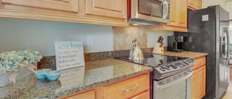 A kitchen with wooden cabinets, a stainless steel microwave, a black refrigerator, a stove, and a kettle.