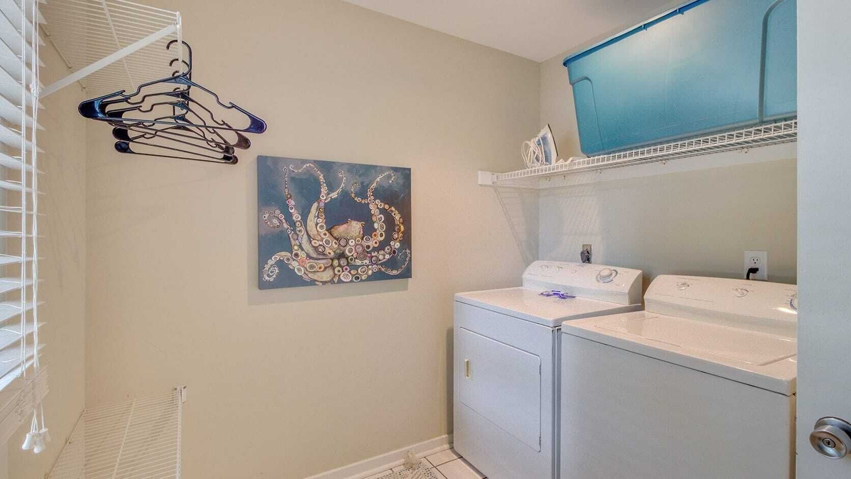 A laundry room with a washing machine, dryer, and a wall-mounted rack with clothes.