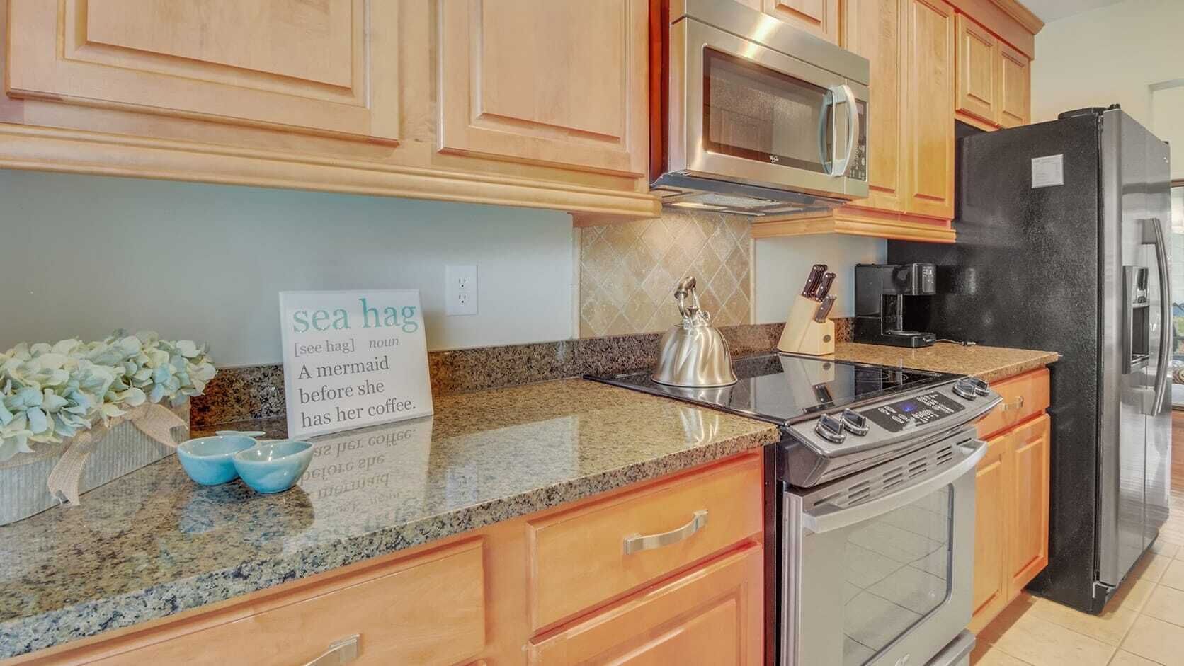 Una cucina con mobili in legno, un forno a microonde in acciaio inossidabile, un frigorifero nero, un fornello e un cartello con l'illustrazione di una sirena.