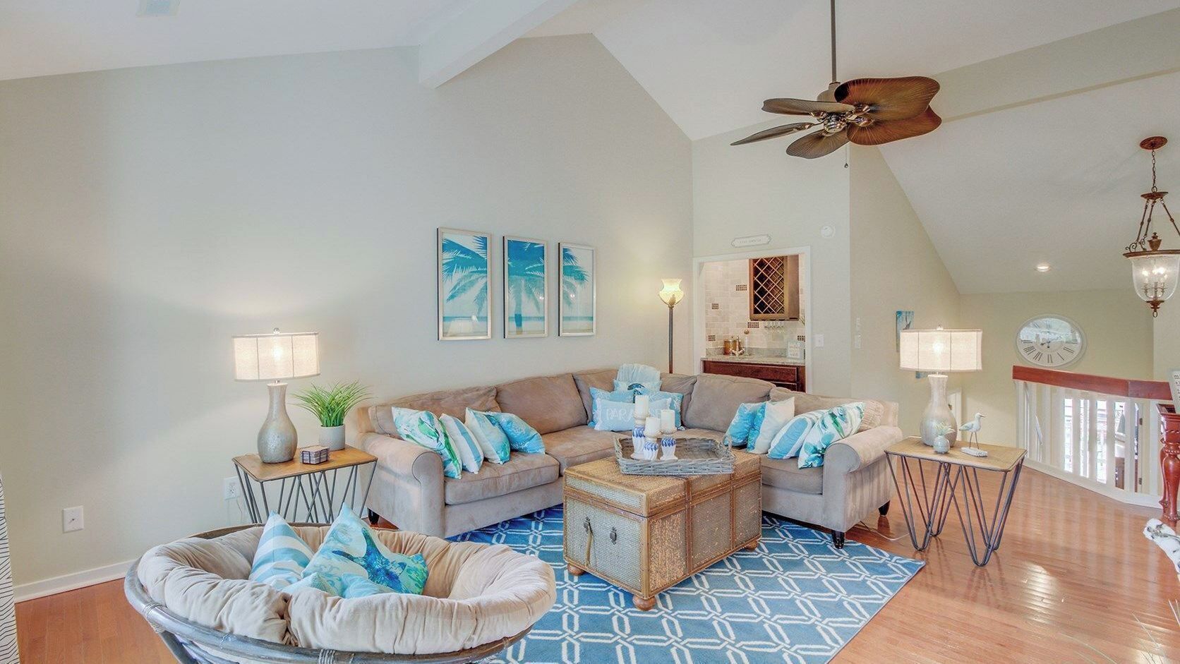 A spacious living room with a high ceiling, a ceiling fan, a dining area with a chandelier, and a staircase leading to an upper level.