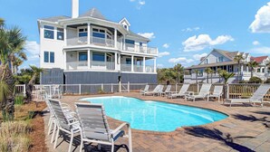 A two-story house with a balcony and a swimming pool surrounded by lounge chairs.
