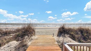 A wooden boardwalk leading to a beach with sand dunes and a clear view of the ocean.