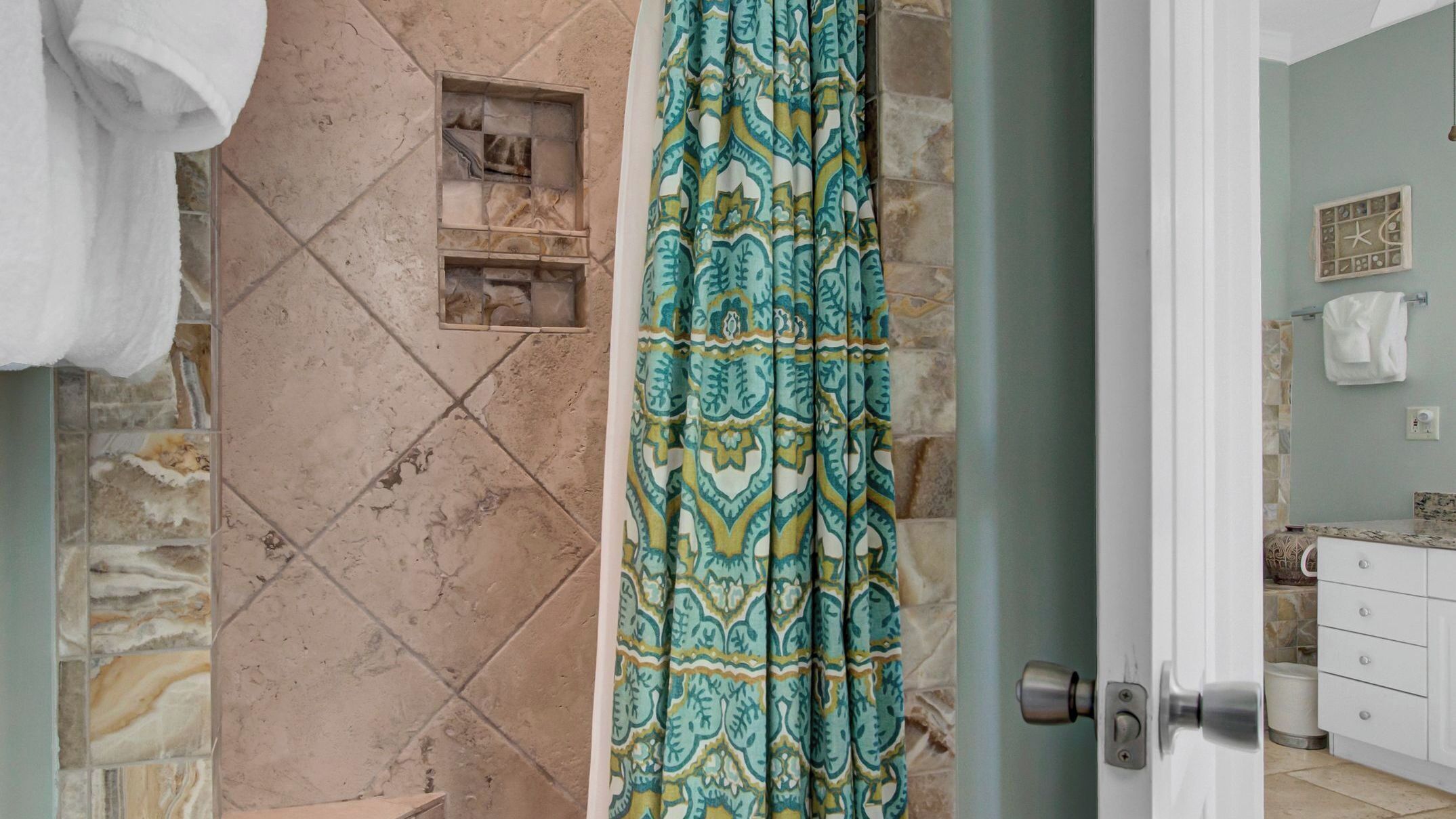 Une salle de bain avec un espace de douche en pierre, un rideau de douche à motifs et un porte-serviettes visible.