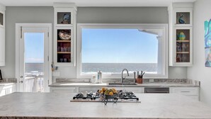 A kitchen with a large window overlooking the ocean, a marble countertop, and a gas stove.