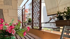 Una mesa de madera con un jarrón de flores rosadas en un balcón que ofrece vistas a edificios.