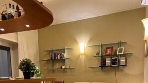 Una sala de estar con sofá, una mesa de centro de madera, una silla y una pequeña cocina con una estantería llena de botellas.