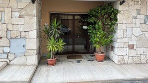 Entrada de un edificio con fachada de piedra, puerta de cristal y dos macetas.