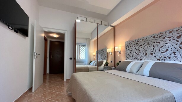 Habitación de hotel con una cama grande, un espejo, un televisor y una puerta que da a otra habitación.