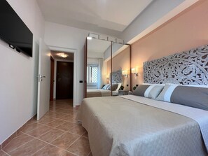 Ein Hotelzimmer mit einem großen Bett, einem Spiegel, einem Fernseher und einer Tür zu einem weiteren Zimmer.