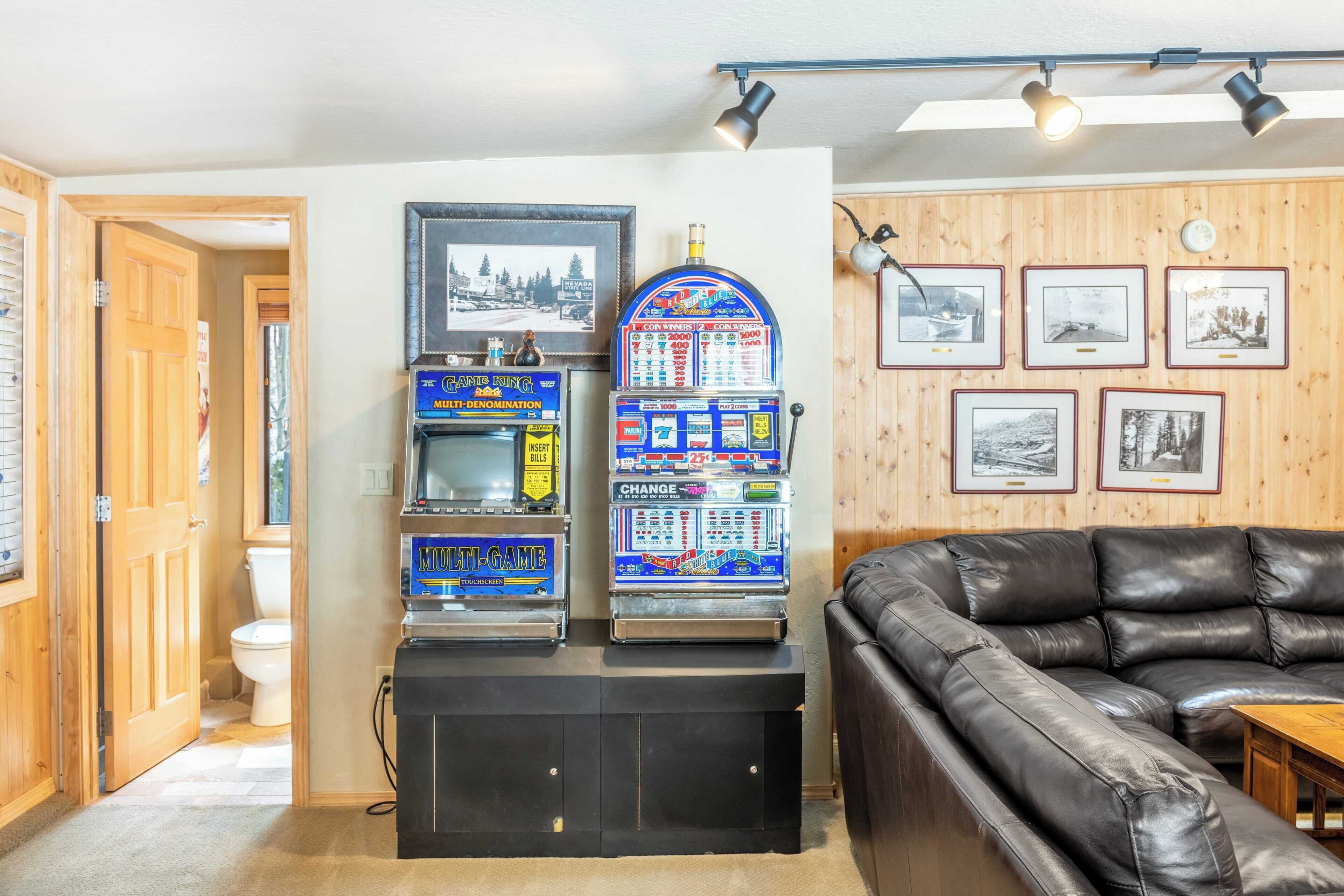 Een woonkamer met een zwarte leren bank, een multifunctionele spelcomputer en ingelijste foto’s aan de muur.