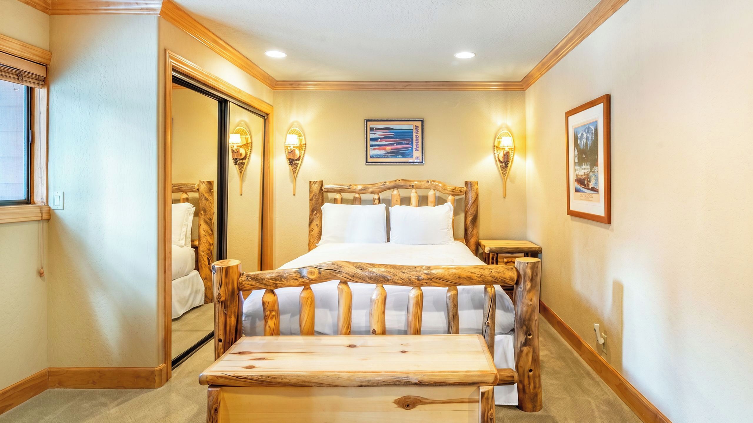 A bedroom with a wooden bed frame, two bedside tables, a bench, and wall-mounted lamps.