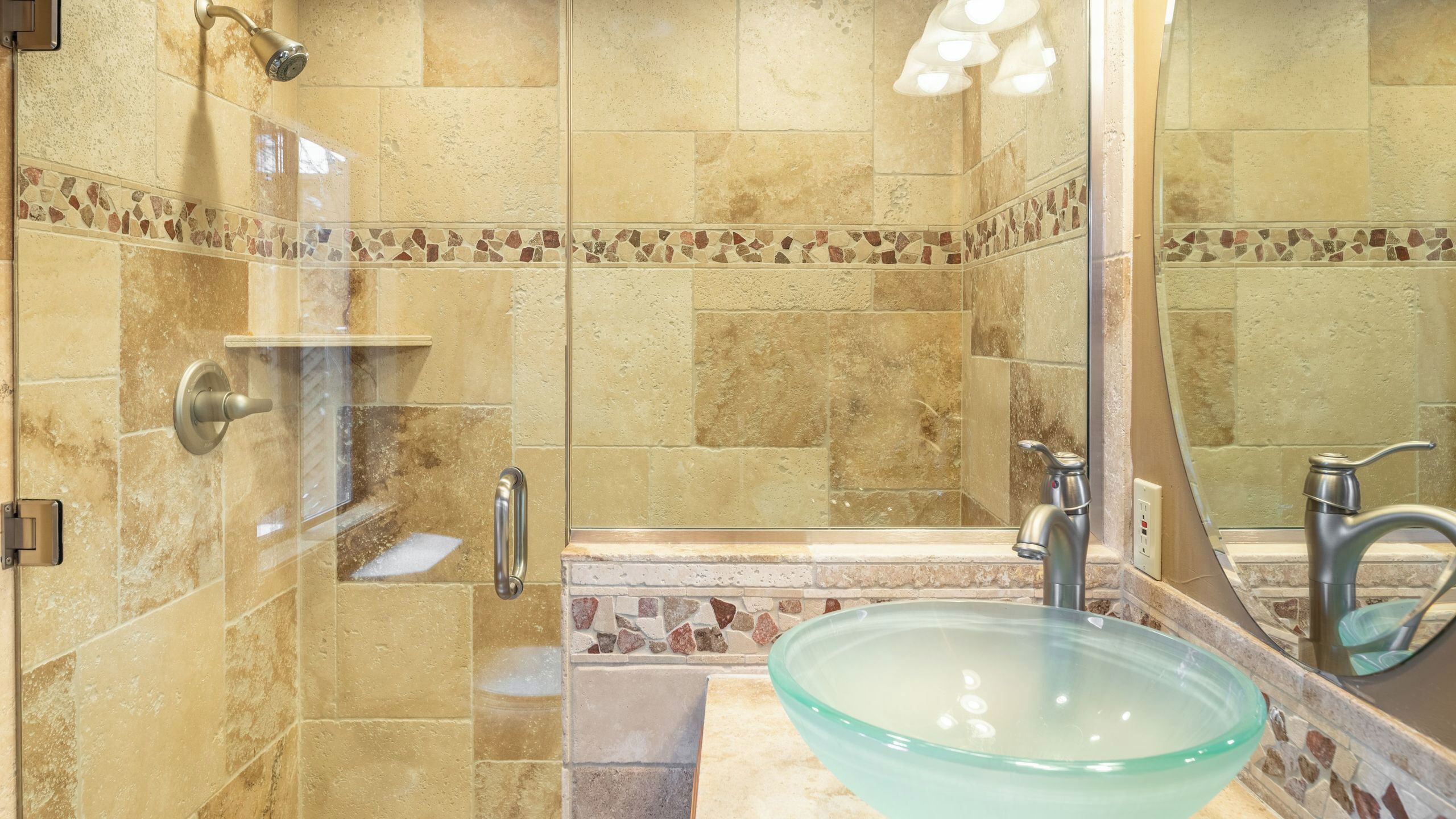 A bathroom with a glass bowl sink, a shower with a handheld showerhead, and a mirror with lights.