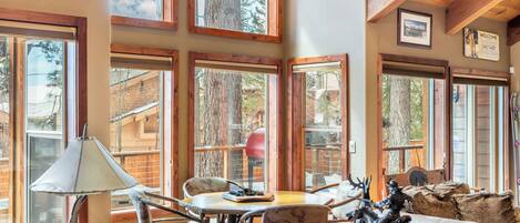 A cozy interior with large windows, wooden beams, and rustic decor including a table, chairs, and animal figurines.