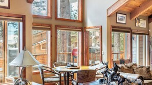 Un interior acogedor con ventanas amplias, vigas de madera y decoración rústica que incluye una mesa, sillas y figuritas de animales.