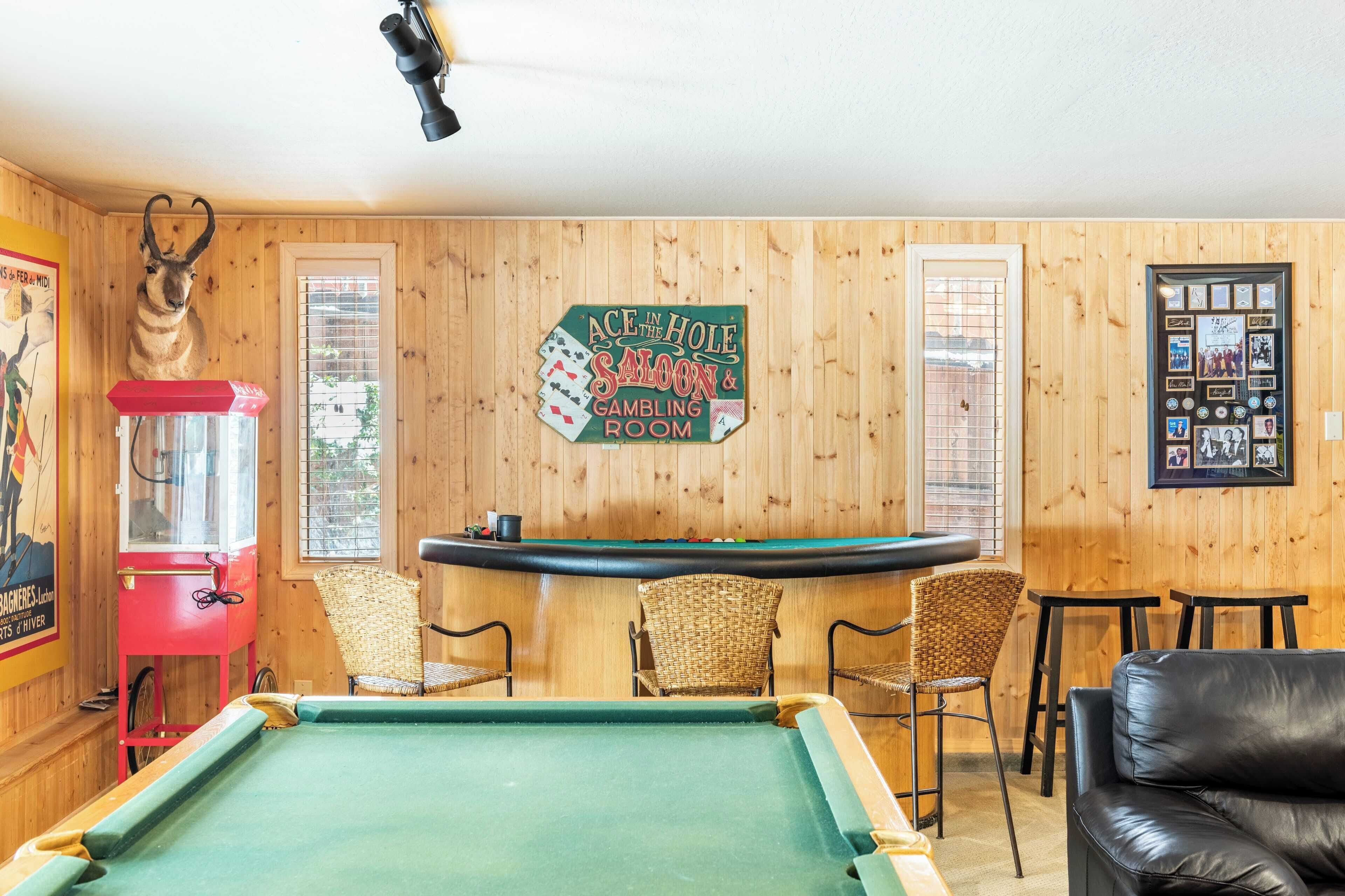 Una mesa de billar en una habitación con paredes de madera, un letrero que dice "Ace in the Hole Saloon & Gambling Room" y una colección de fotos enmarcadas en la pared.