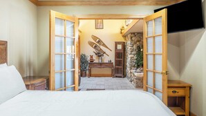 Een hotelkamer met een bed, een houten nachtkastje, een bureau met stoel, een stenen muur en een aan de muur bevestigde televisie.