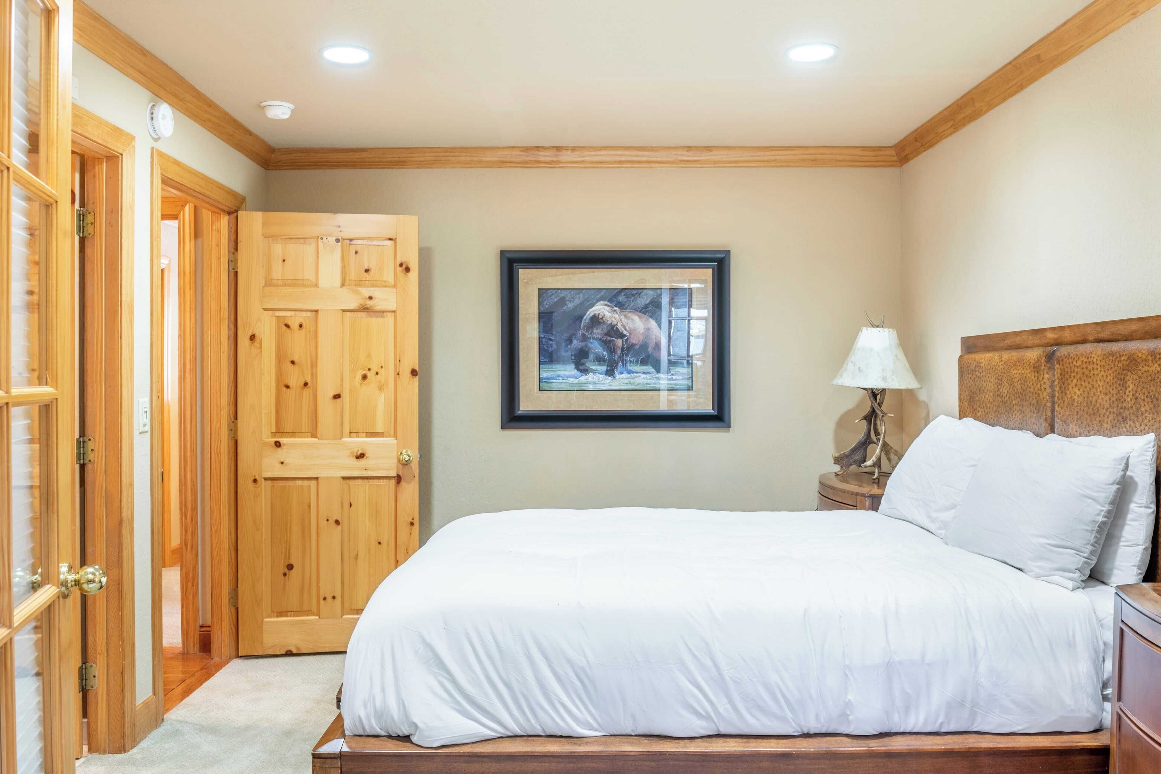 Quarto com cama de madeira, quadro pendurado na parede e porta de madeira.